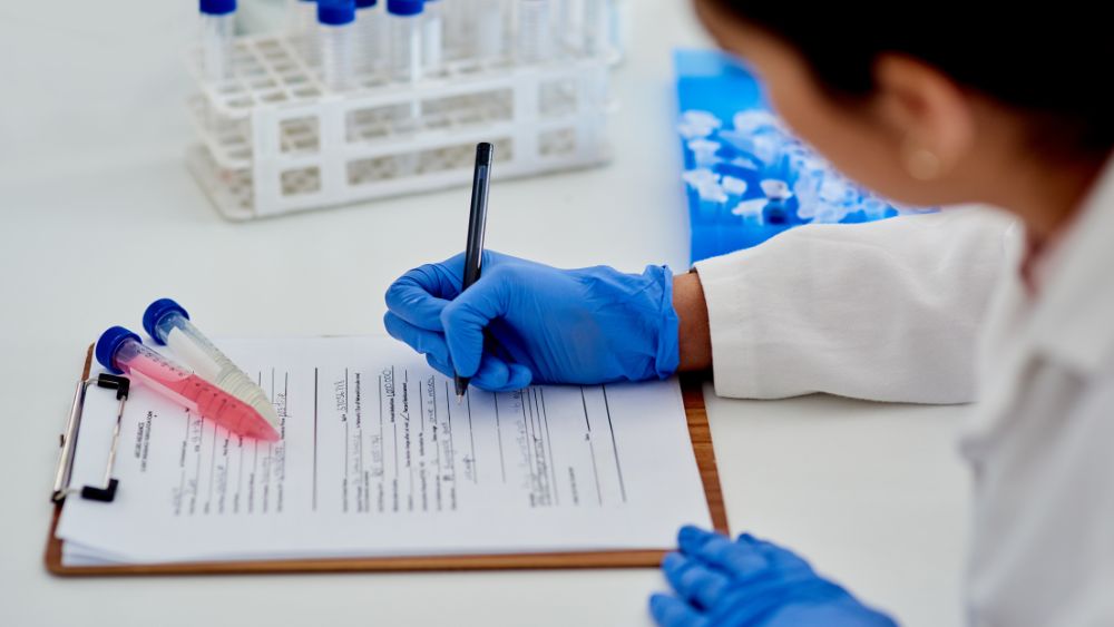 Lab technician recording blood test results on a medical report with sample tubes in a diagnostic laboratory.
